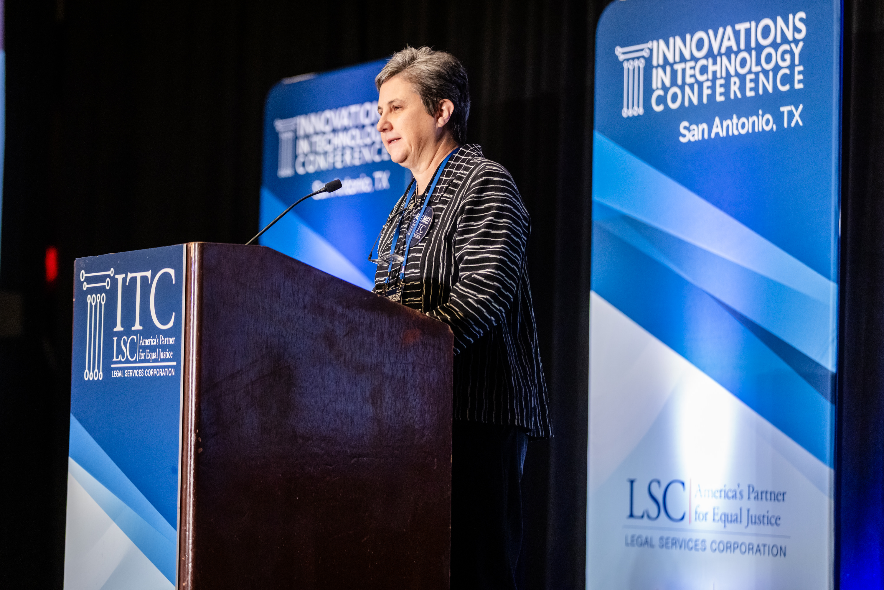 Speaker at an ITC podium framed by blue Innovations in Technology Conference banners